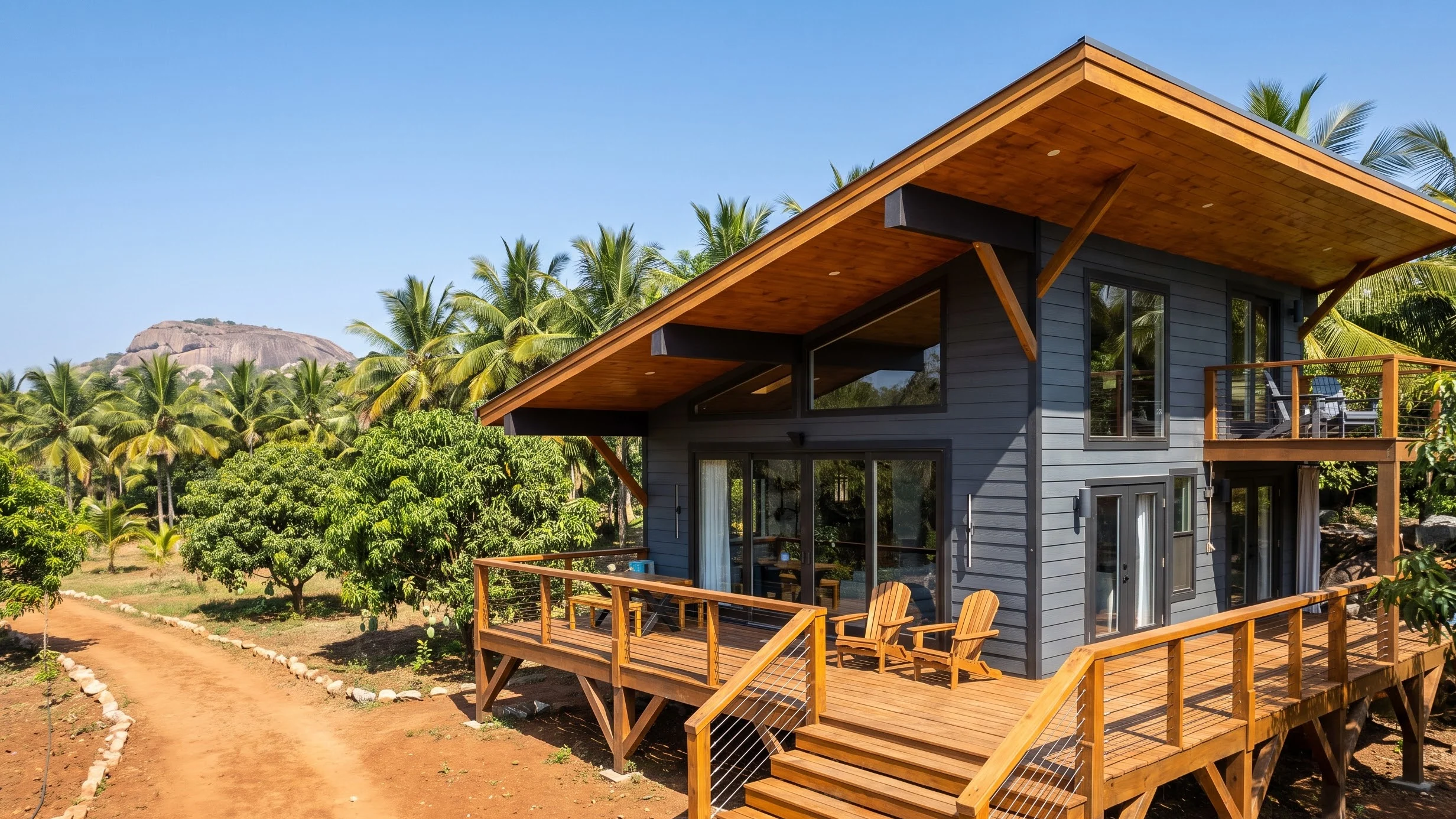 A modular farm cottage with a sloped timber roof and a wrap-around deck, among mango trees and coconut palms