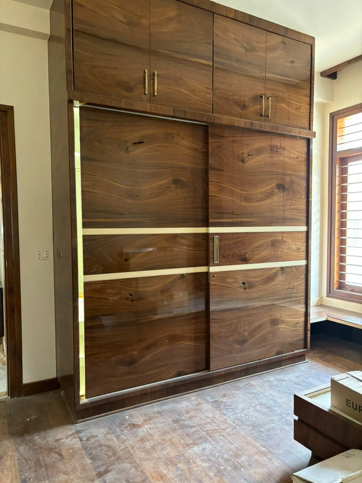 A full-height bedroom wardrobe in a walnut finish with two sliding doors, cream inlay bands and lofts above
