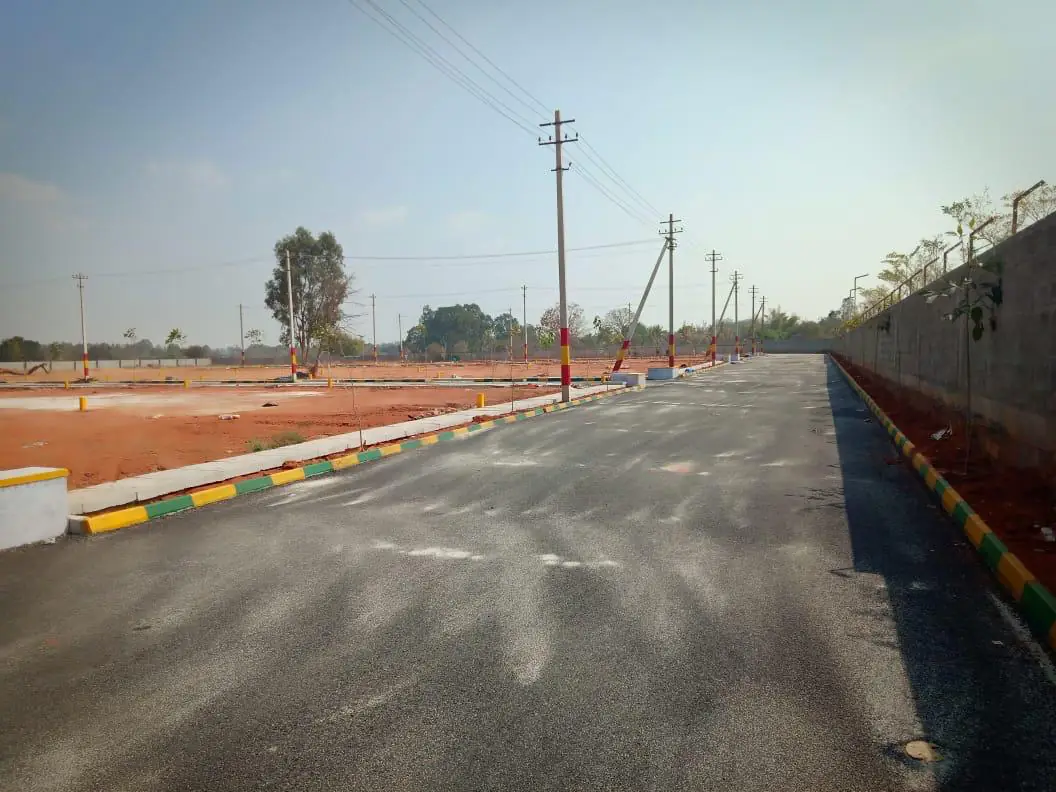 An asphalt layout road with yellow and green painted kerbs, street-light poles along it and a compound wall at the far end