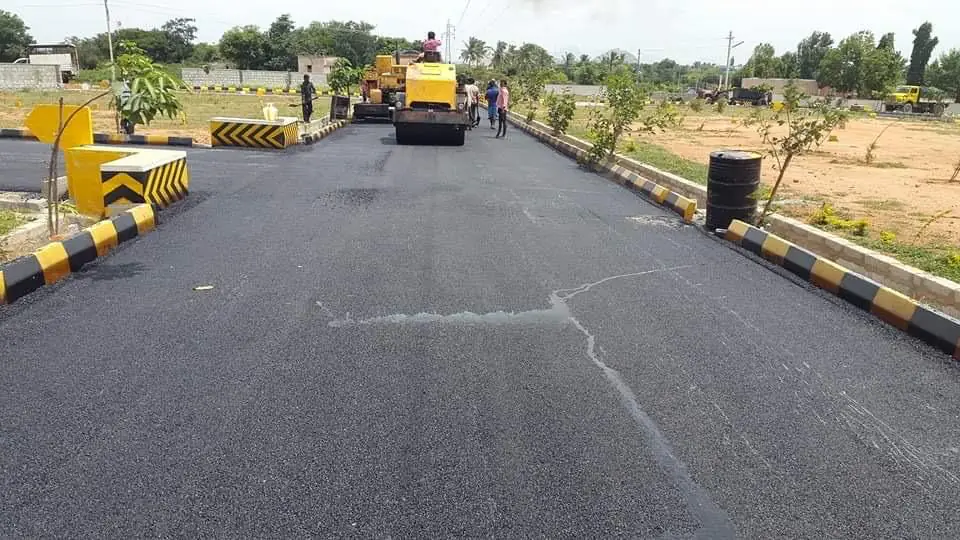 A paver and a road roller laying asphalt on a layout road between painted kerbs