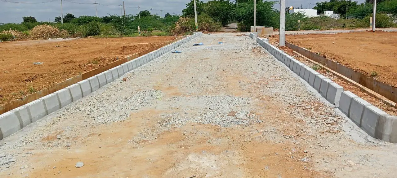 A road bed of crushed stone between two lines of kerb, with levelled plots on both sides