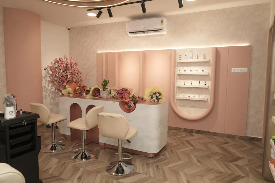 A marble-look counter with arched cut-outs and three stools, in front of fluted blush-pink panels and a lit display shelf
